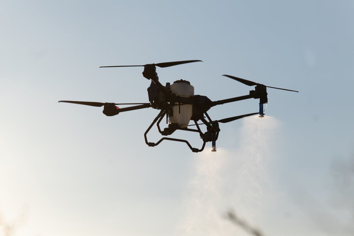 EAVision J70 spray drone in flight against a bright sky, four rotors turning and spray nozzles running