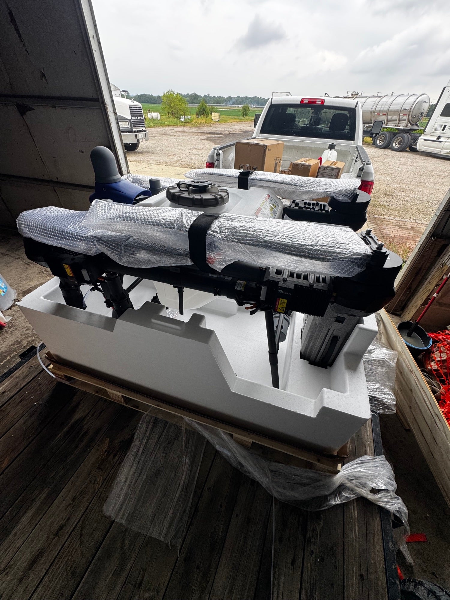 EAVision J150 spray drone lifted out of its crate onto a trailer, still wrapped, with the Premium Ag Services truck parked behind